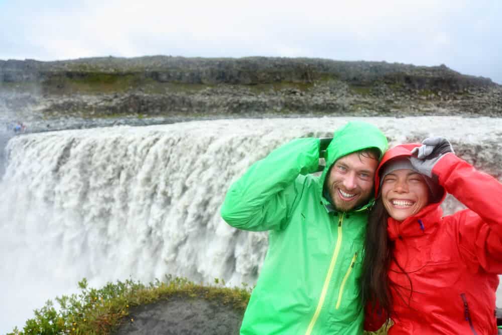 Couple in colored rain jackets enjoying Dettifoss waterfall
