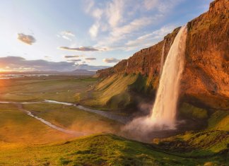Midnight sun in Iceland on the horizon with a waterfall