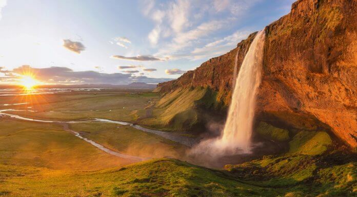 Midnight sun in Iceland on the horizon with a waterfall